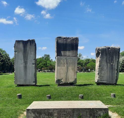 Three large stone monuments stand in a grassy area under a blue sky with clouds.