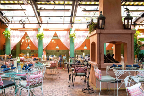 Brightly lit restaurant interior with colorful tables, chairs, and decorative plants, featuring a cozy fireplace.