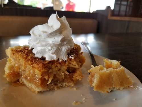 A slice of dessert topped with whipped cream, served on a plate with a fork and a bite taken out.