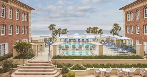 A serene beachfront hotel with a pool, lounge chairs, and palm trees under a cloudy sky.