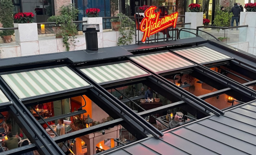 View of a rooftop restaurant called "The Hideaway," featuring striped awnings and festive decorations.