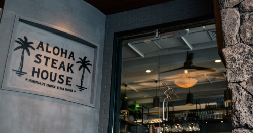 Sign for Aloha Steak House with palm trees, showcasing a welcoming entrance to the restaurant.