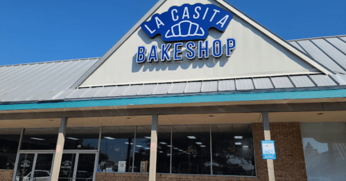 Exterior of La Casita Bakeshop, featuring a blue sign and large windows under a clear blue sky.