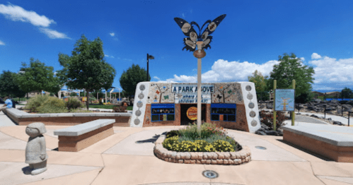 Colorful park entrance with a butterfly sculpture, surrounded by flowers and greenery under a bright blue sky.