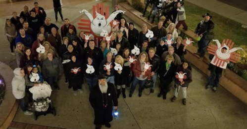 A large group of people gathered outdoors, holding signs with cartoonish white rabbits and red handprints.