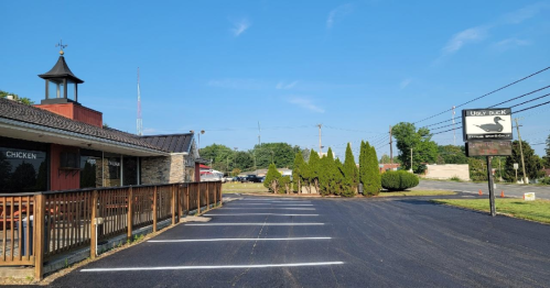 A restaurant exterior with a wooden deck, sign, and neatly lined parking spaces under a clear blue sky.