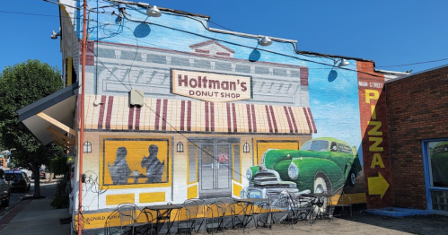 Mural of Holtman's Donut Shop featuring a vintage car and outdoor seating in a vibrant, colorful setting.