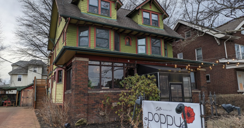A colorful, three-story house with a sign for "Poppy" restaurant in front, surrounded by trees and other buildings.