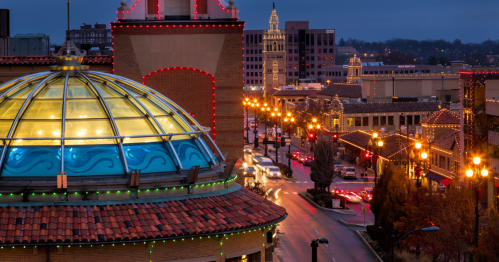 A cityscape at dusk featuring a domed building with colorful lights and a busy street lined with illuminated buildings.