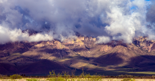 Dramatic mountain landscape with clouds hovering over peaks and shadows cast on the valley below.