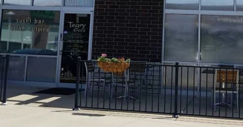 Exterior of a sushi bar with a sign, featuring a flower planter and outdoor seating.