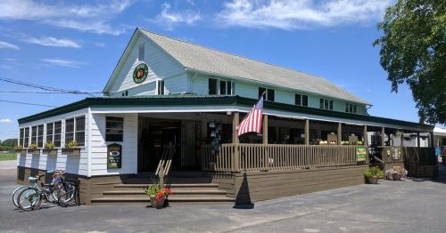 A charming white restaurant with a porch, American flag, and bicycles parked outside, set against a clear blue sky.