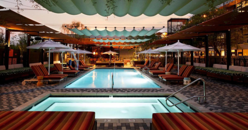 A stylish pool area with lounge chairs, umbrellas, and colorful canopies, illuminated at dusk.
