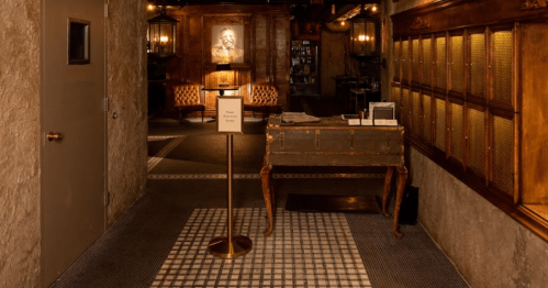 A dimly lit hallway with vintage decor, featuring a reception desk and seating area in the background.