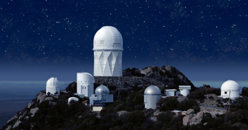 A mountain observatory with multiple domes under a starry night sky.