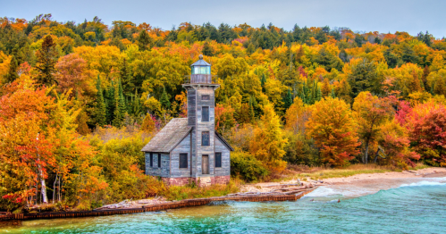 A scenic lighthouse by a colorful autumn forest, with vibrant fall foliage and a calm shoreline.
