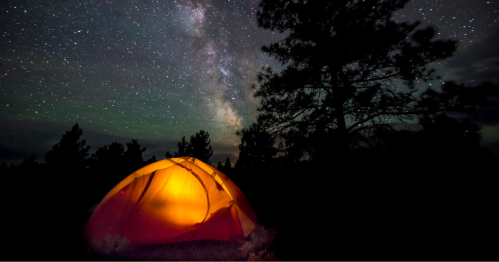A glowing orange tent under a starry night sky with the Milky Way visible in the background.