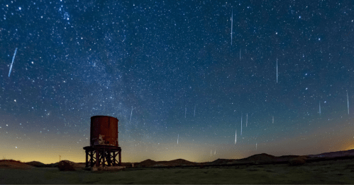 A starry night sky with shooting stars above a water tower in a desert landscape.