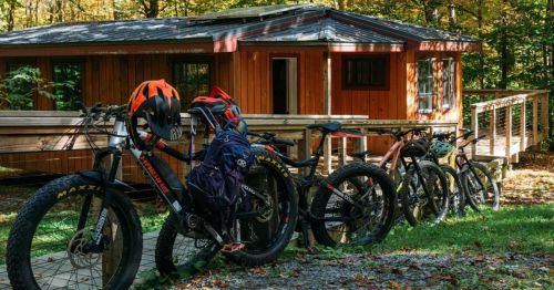A row of mountain bikes parked in front of a wooden cabin surrounded by autumn foliage.