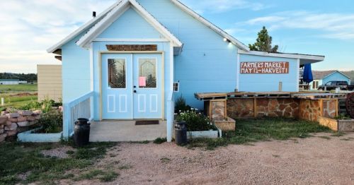 A light blue building with a sign reading "Farmers Market" and a welcoming entrance surrounded by greenery.