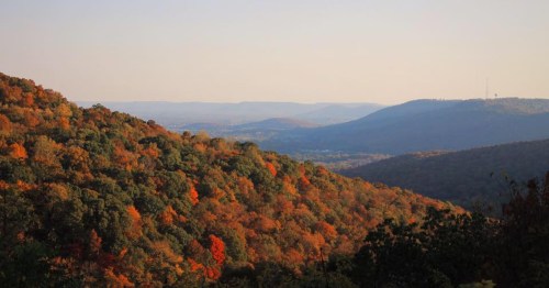 A scenic view of rolling hills covered in vibrant autumn foliage under a clear sky.