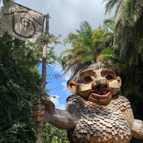 A large wooden troll sculpture holding a flag, surrounded by lush greenery and trees.