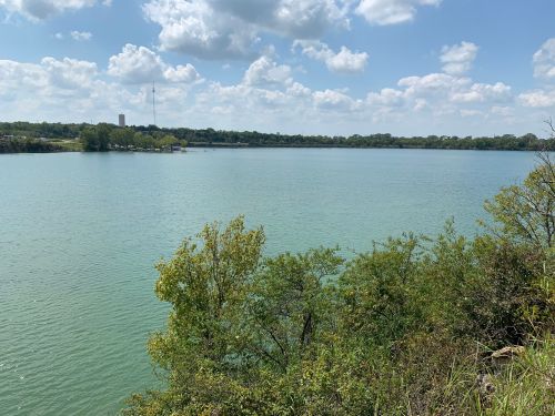 A serene lake surrounded by greenery under a partly cloudy sky.