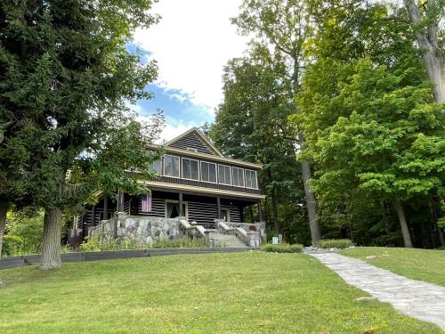 A large wooden house with a stone foundation, surrounded by trees and a grassy path leading to it.