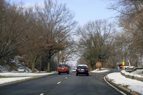 A snowy road lined with bare trees, featuring two cars driving in opposite directions.