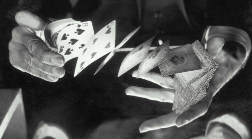 A close-up of hands fanning out playing cards, showcasing various suits and numbers in black and white.