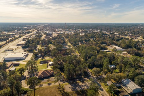 Aerial view of a small town with roads, buildings, and trees under a clear blue sky.