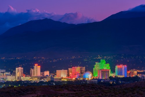 A vibrant city skyline at dusk, featuring colorful illuminated buildings against a mountainous backdrop.