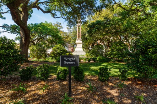 A park scene featuring a monument surrounded by trees and shrubs, with a sign reading "Wright Square" in the foreground.