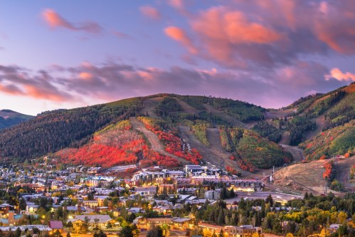 A scenic view of a mountain landscape with vibrant autumn foliage and a town nestled in the valley below.