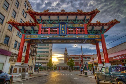 Colorful Chinese archway at sunset, framed by buildings in an urban setting, with a clock tower in the background.