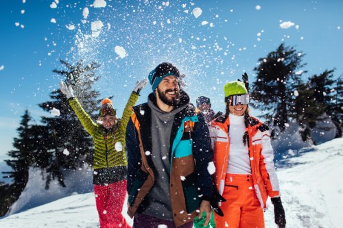 A group of friends joyfully playing in the snow, wearing colorful winter gear against a bright blue sky.
