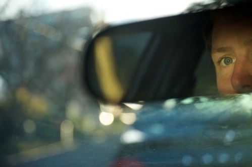 A close-up of a person's eye reflected in a car's side mirror, with a blurred background and soft lighting.