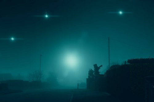 A foggy street scene at night, illuminated by a bright light and mysterious orbs in the sky.