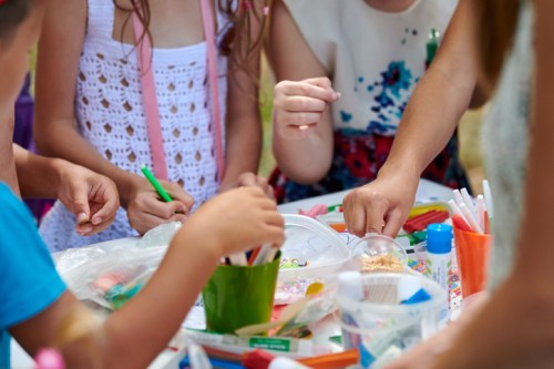 Children's hands engaged in arts and crafts, surrounded by colorful markers, paper, and various craft supplies.