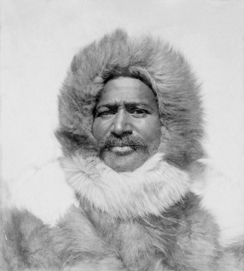 A man in a fur-lined parka with a hood, smiling against a snowy background.