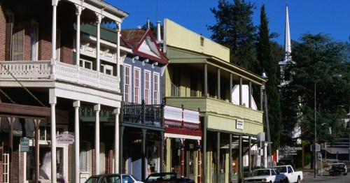 Historic buildings line a street, featuring colorful facades and a church steeple in the background under a clear blue sky.