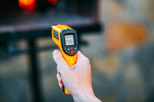 A hand holding a yellow infrared thermometer displaying a temperature of 98.8°F.