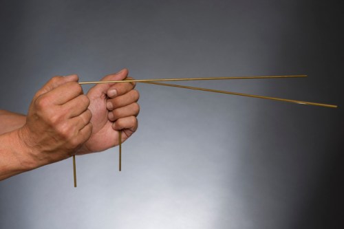 A person's hands hold two long, thin metal rods against a dark background.
