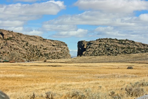 A wide landscape featuring rocky cliffs flanking a grassy valley under a blue sky with scattered clouds.