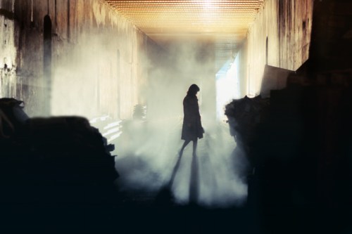 A silhouette of a person stands in a foggy corridor, with light streaming in from one side.