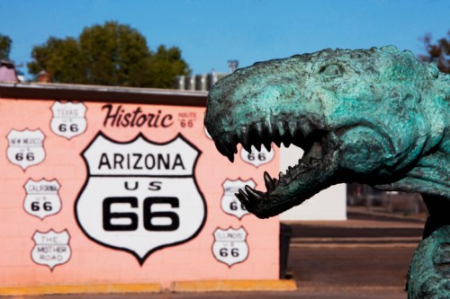 A bronze dinosaur statue in front of a colorful Route 66 sign in Arizona.