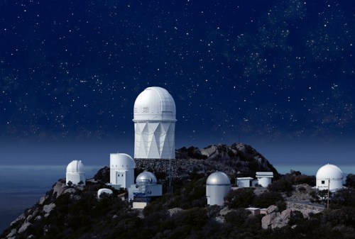 A group of white observatories on a mountain under a starry night sky.