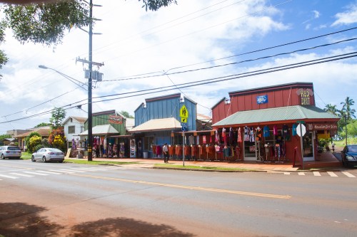 Colorful storefronts line a street, with clothing displays and a clear blue sky overhead.