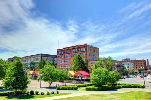 A vibrant cityscape featuring colorful buildings and trees under a blue sky with scattered clouds.
