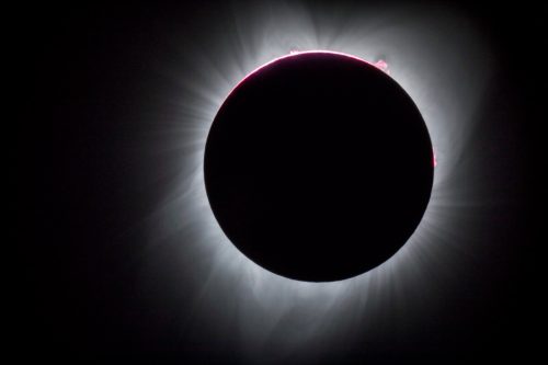 A solar eclipse with a darkened sun surrounded by a glowing corona and faint solar flares.